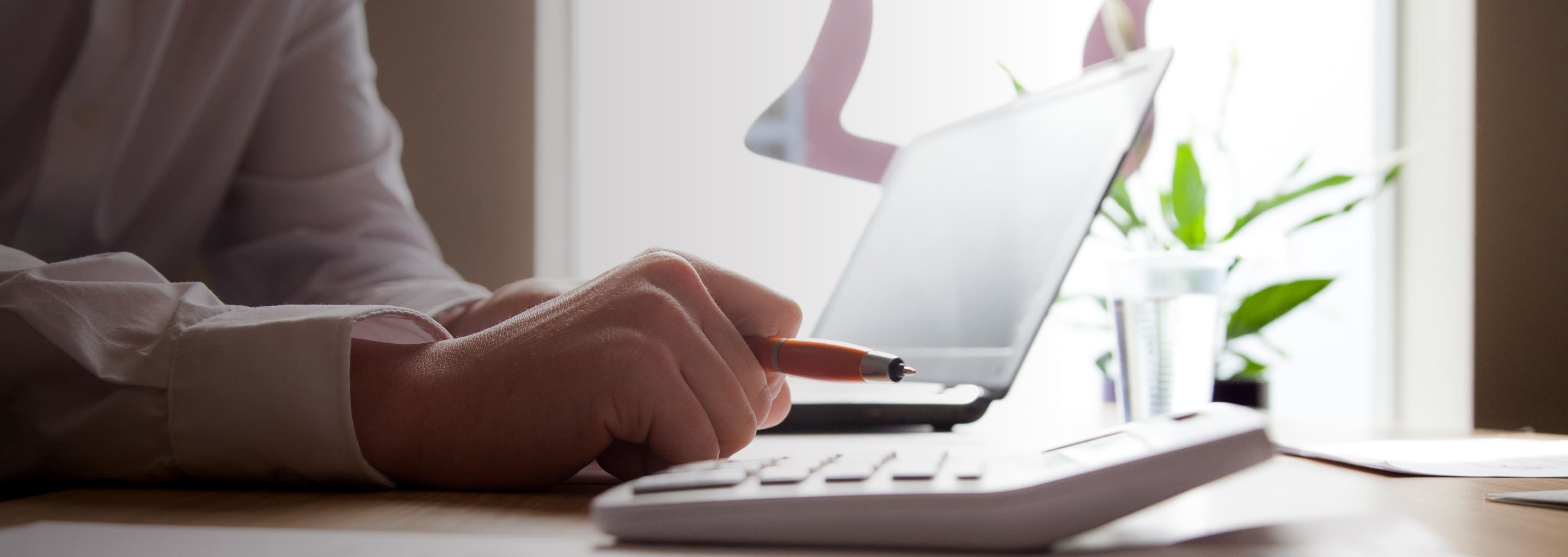 male working on laptop with pen in hand