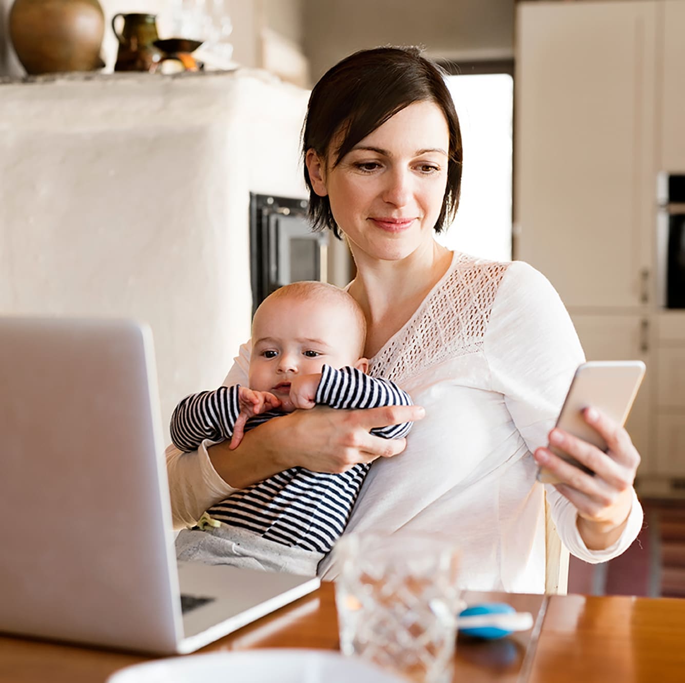 woman holding her baby in her arms while she's holding a mobile phone